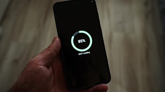 Circular progress ring at 53 percent with 2027 Loading below it, displayed on a smartphone held in one hand in a dim room with a wooden backdrop. It shows the new year halfway there, progress trackin