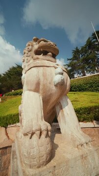 Slow-motion pan across a traditional Chinese guardian lion statue under bright blue sky.