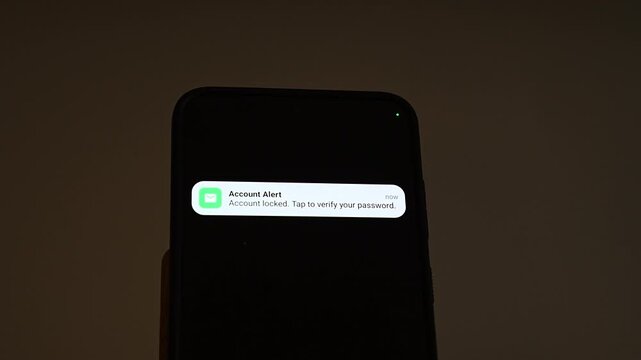 An Account Alert notification slides onto a smartphone in a dark room, claiming the account is locked and asking the user to tap and verify the password. A typical phishing lure for credential theft 