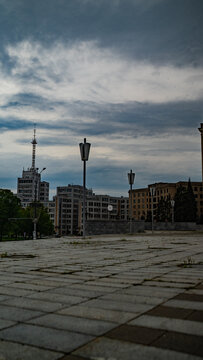 Constructivist architecture and iconic high rise buildings in a city square under a cloudy sky.