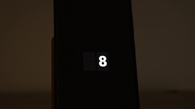 White flip clock digits count down from 10 to 0 on a smartphone standing in a dark, warm room, then HAPPY NEW YEAR appears. A timeless midnight countdown for any year, New Year Eve parties and celebr