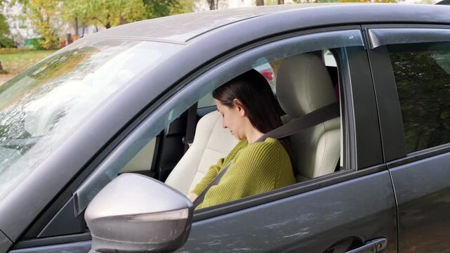 Female driver fastens seatbelt securely inside modern car before starting commute journey, demonstrating essential road safety habits with calm focus from driver seat position outdoors.