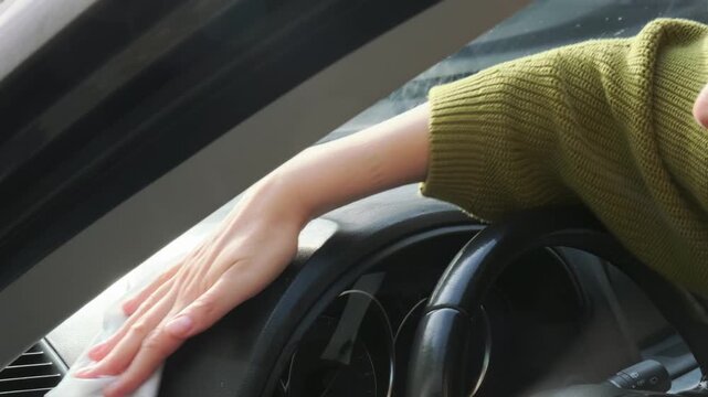 Careful motorist wipes vehicle panel steadily with damp cloth, cleaning dusty dashboard surface inside cabin, maintaining sanitary car interior atmosphere through diligent hand scrubbing