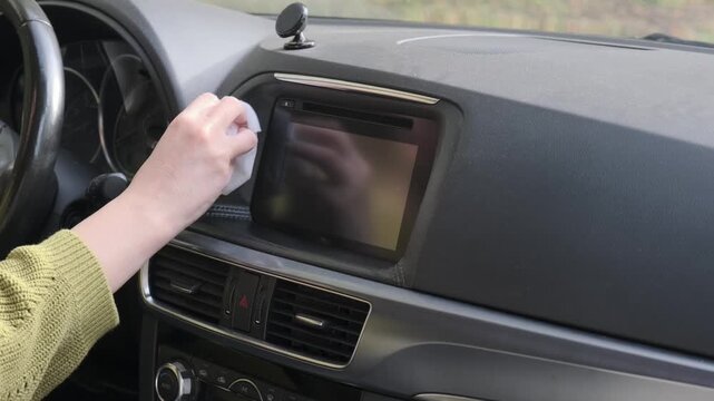 Female driver wipes car panel with damp cloth carefully while cleaning vehicle dashboard interior screen removing accumulated dust during regular maintenance routine inside automobile cabin