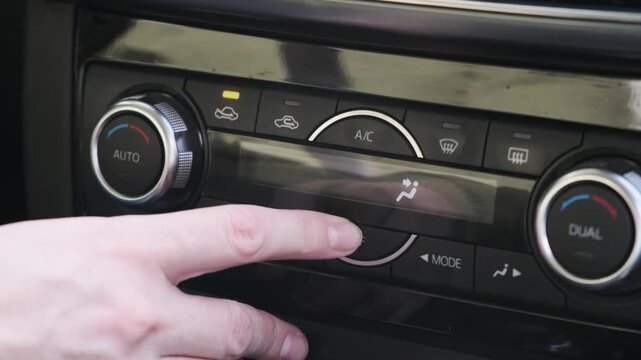 Automobile driver shuts off air conditioning system using central dashboard buttons, reaching out to push power control key on digital climate panel while seated in modern vehicle interior