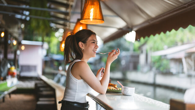 Young asian woman eating pad thai at a riverside restaurant in khlong bang luang Bangkok local travel