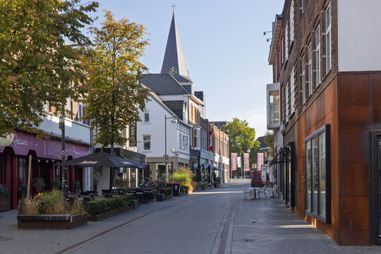 Heerlen, Netherlands - October 04, 2026: Quiet shopping street with cafes, restaurants, shops and view towards Sint Pancratiuskerk church tower.