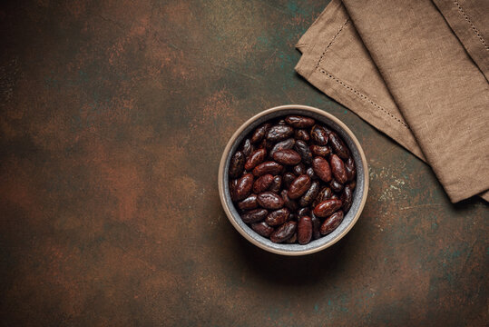 Bowl of cocoa beans on a dark grunge background, top view, copy space