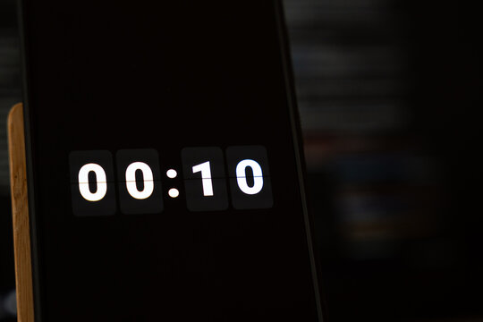 Ten second countdown showing 00:10 on a smartphone flip clock timer with white digits on black, dark background and wooden stand, concept of final countdown, new year countdown and launch event