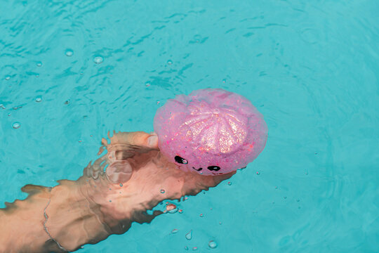 Child's hand holding a pink squishy dumpling toy in clear water, playful sensory experience, stress relief, tactile exploration, satisfying textures and creative childhood fun