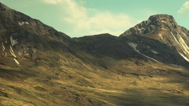 Vast mountains loom over a sprawling green valley, bathed in sunlight. The rugged terrain showcases natural beauty, with patches of snow highlighting the rocky surfaces.