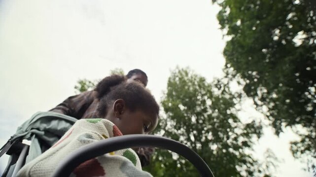 African American mother talking to child sitting in stroller from low angle outdoors. Clip fits parenting commercials, maternity healthcare promos, and modern family lifestyle projects