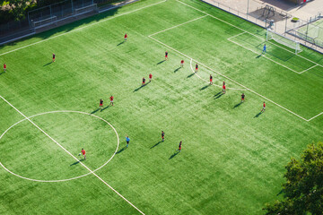 Fototapeta premium Aerial drone view of a football match on a green field. Players competing during a sports game on a stadium pitch.