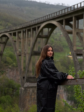 Young female tourist in black raincoat looking at camera near Djurdjevica Tara Bridge