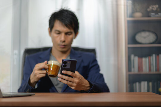 Young Man Relaxing at Home Drinking Coffee and Using Smartphone