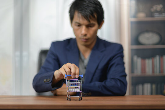 Young man in formal blazer pushing small shopping cart on wooden table in indoor setting