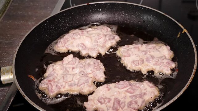 Diced meat and pieces of dough cooking together in a frying pan during homemade meal preparation.