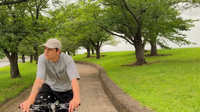 Young man riding a bicycle along a park path surrounded by green trees, Japan