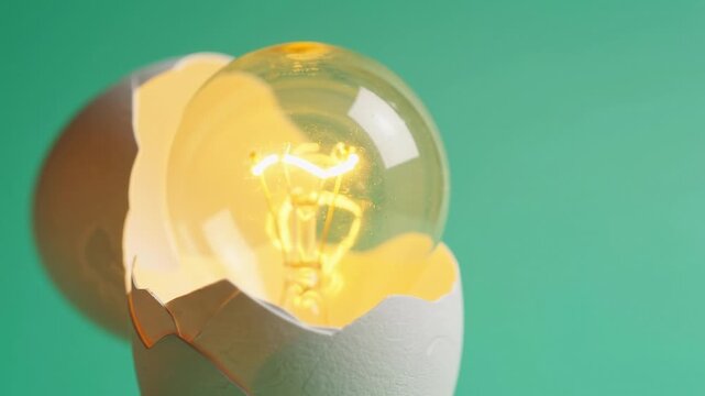 Glowing light bulb inside a cracked white eggshell on a green background represents a surreal concept of a bright idea hatching from an egg in this creative studio shot.