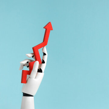 A white robotic hand holding a red upward arrow chart against a light blue background. Concept of artificial intelligence analyzing cryptocurrency market, exchange trends, growth and financial success