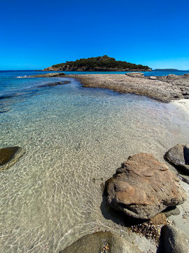 Vertical Scenic view of turquoise transparent sea and sandy shore with Farina island in background, near Porto-Vecchio, Corsica, France. Beautiful Mediterranean summer landscape.