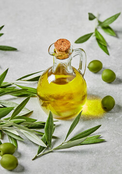 Olive oil bottle with fresh olives and branches on gray surface