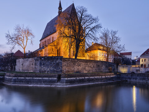 St Gothard Church above a pond and stone wall at dusk in Slany