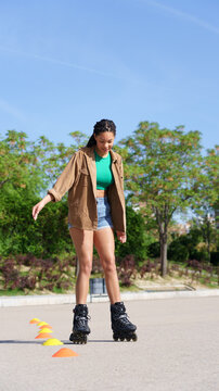 Young woman roller skating slalom cones outdoors