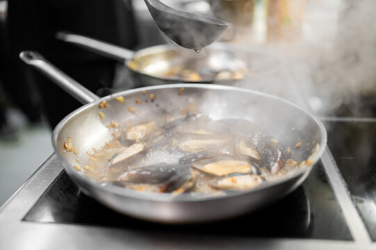 Mussels cooking in a stainless steel pan with garlic and white wine sauce on an induction stove.