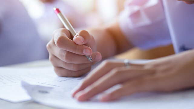 Extreme Close-up of Student Hand Holding Pen Writing Exam Paper on Desk