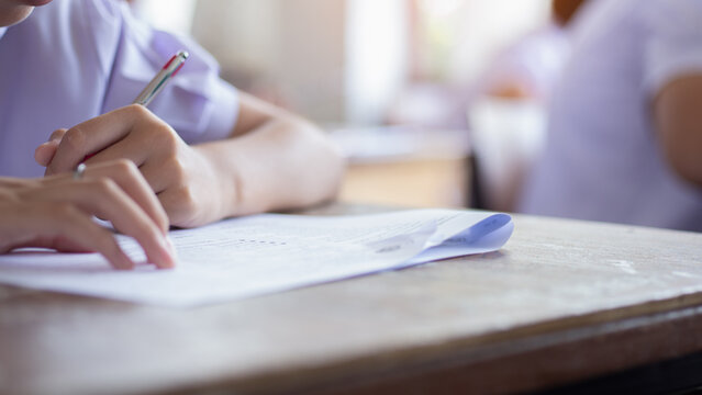 Close-up of Student Hand Holding Pen Writing Exam Paper on Desk