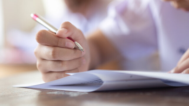 Close-up of Student Hand Holding Pen Writing Exam Paper on Desk