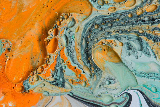 Abstract fluid art macro texture with vibrant orange paint swirls and turquoise bubbles.