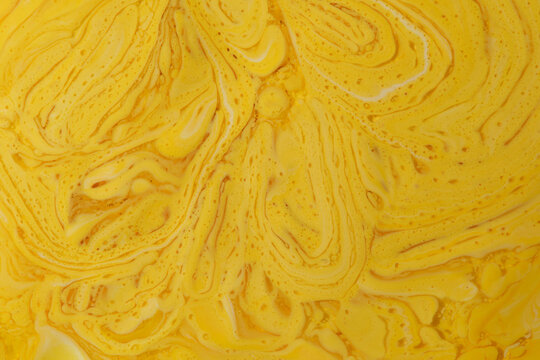 Close up rich yellow fluid paint mixture with detailed bubbly, cellular, and swirling textures.