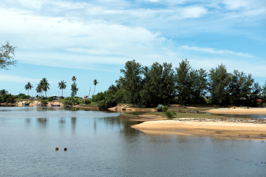 Kuala Kemasik Coastal Lagoon, Terengganu, Malaysia - Coastal landscape with calm lagoon water, sandy banks, tropical vegetation, coconut palms, and a bright blue sky creating a serene natural setting.