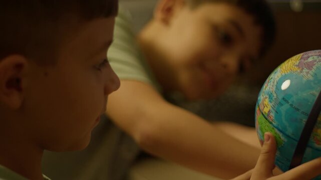 Two young boys explore a globe with curiosity. One smiles warmly while the other studies the map intently. They share a quiet moment of learning and wonder