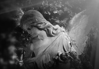 Fototapeta premium Stone angel holding roses illuminated by heavenly light, symbolizing hope, remembrance, eternal peace and the journey of the soul to heaven.