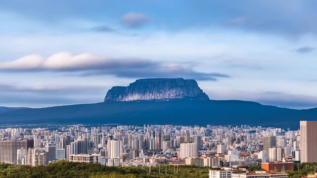 Panning aerial slow motion of city skyline with flat top mountain overlooking urban valley at dawn