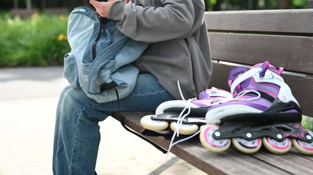 Skater wears knee pads, sits on park bench.