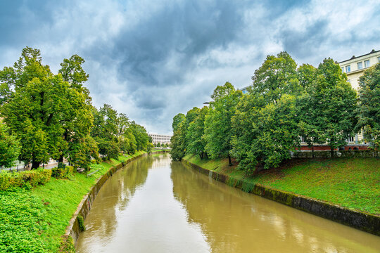 Ljubljana river channel flowing through the city center with green trees and historic buildings under a cloudy sky in Slovenia