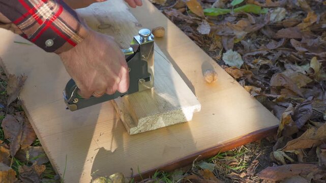 A man tests a construction stapler on a wooden board. Worker checking heavy duty staple gun on wood plank