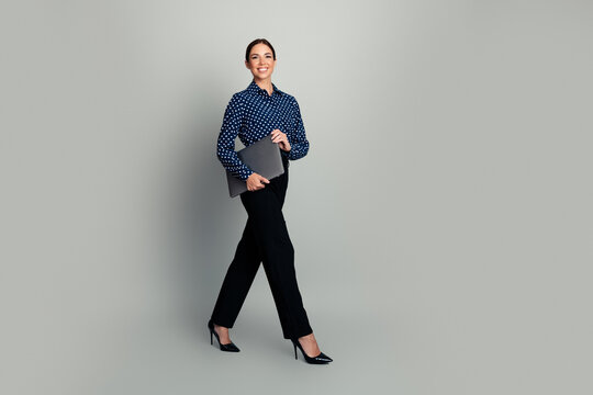 Confident businesswoman walking with laptop in hand wearing polka dot blouse and heels for corporate portrait and professional lifestyle concept