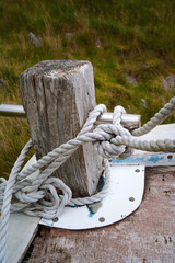 A white mooring rope wraps around a wooden post above a worn boat deck on Lewis and Harris, Outer Hebrides, Scotland. © George
