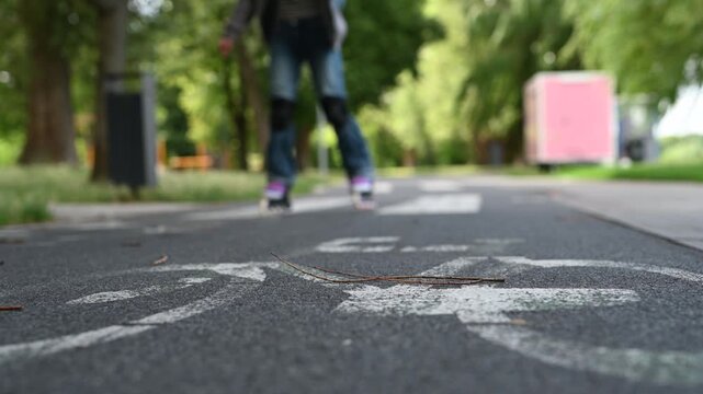 Young girl with blonde hair inline skates on a paved park path during daytime.