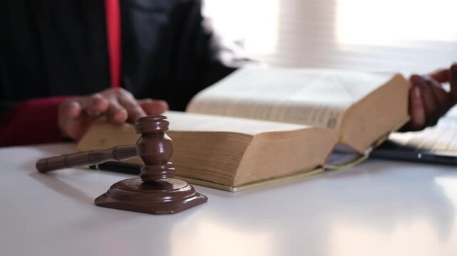The judge opened a large reference book to consult the legal articles pertaining to the crime before pronouncing the sentence upon the offender in the courtroom.