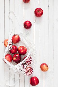 Vertical flat lay of red apples in white mesh eco bag on wooden planks. Top view zero waste shopping concept with fresh organic fruits on background, perfect for sustainable lifestyle design.