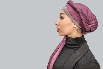 Side shot of young arabian woman in hijab. She stands alone. Isolated on grey background.