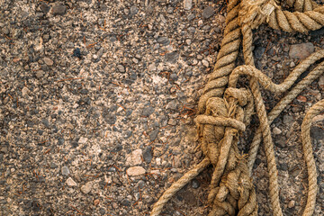 Top-down view of thick knotted hemp rope coiled on a rough, gravelly asphalt surface. © Bits and Splits