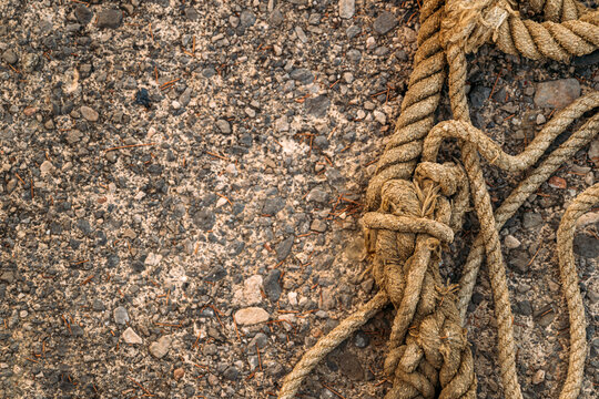 Top-down view of thick knotted hemp rope coiled on a rough, gravelly asphalt surface.