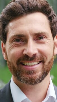 Close-up portrait of a smiling adult man looking at the camera outdoors. Positive male face expression in natural daylight on a city street. Handsome mature man showing happiness, confidence, and